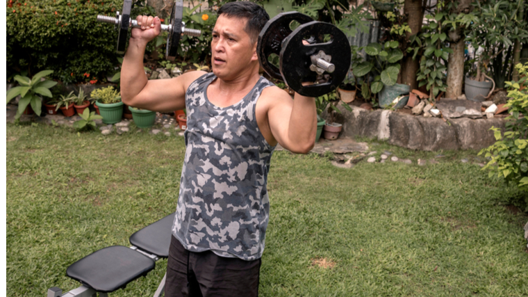 Man exercising outdoors holding dumbbells near shoulders