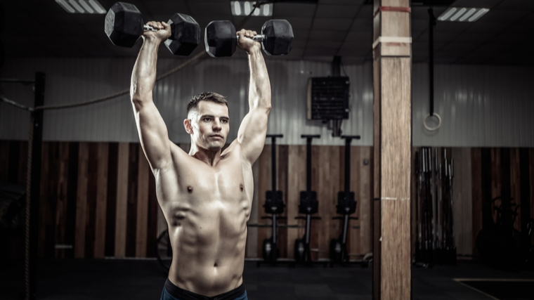 Muscular man in gym pressing dumbbells overhead
