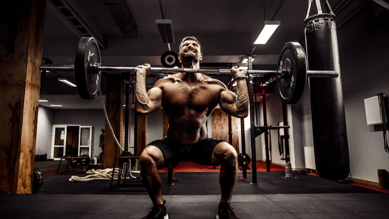 very muscular man straining while holding a barbell and squatting