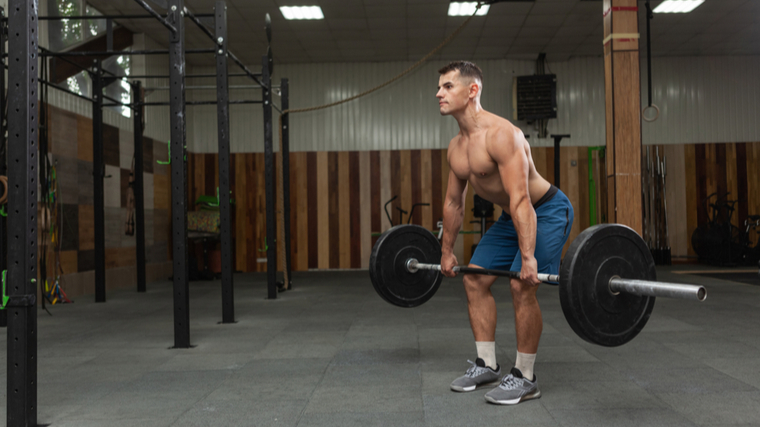 Man in empty gym performing barbell deadlift