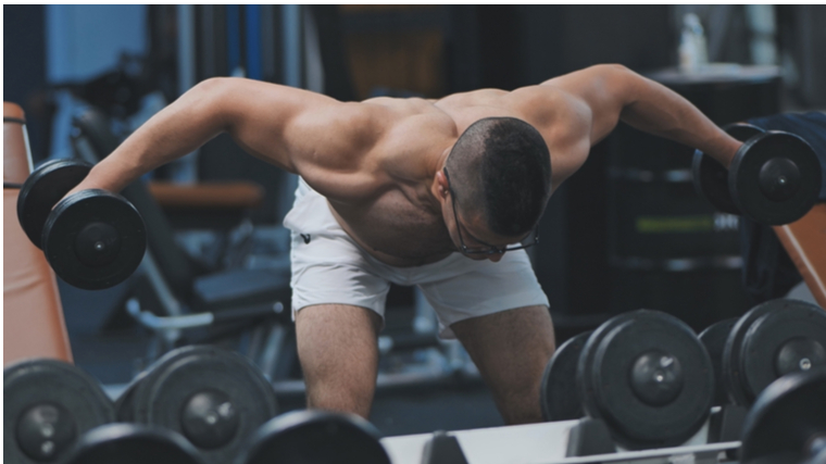 Muscular man in gym performing dumbbell shoulder exercise