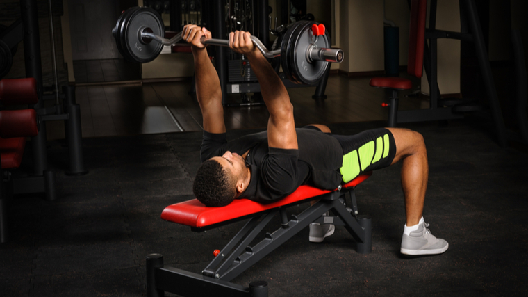 Man in gym lying on bench performing barbell exercise